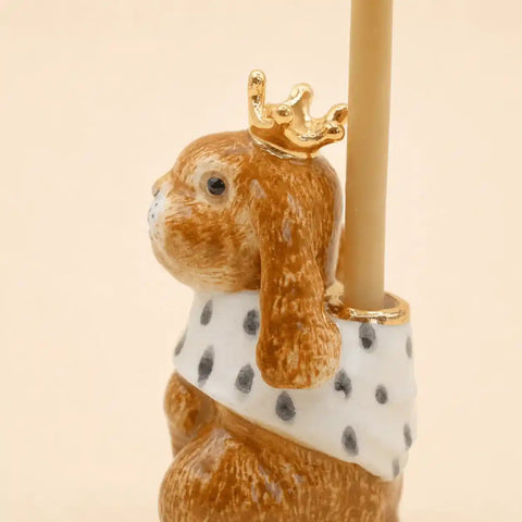 Ceramic rabbit figurine with a gold crown and polka dot scarf holding a candle on a beige background