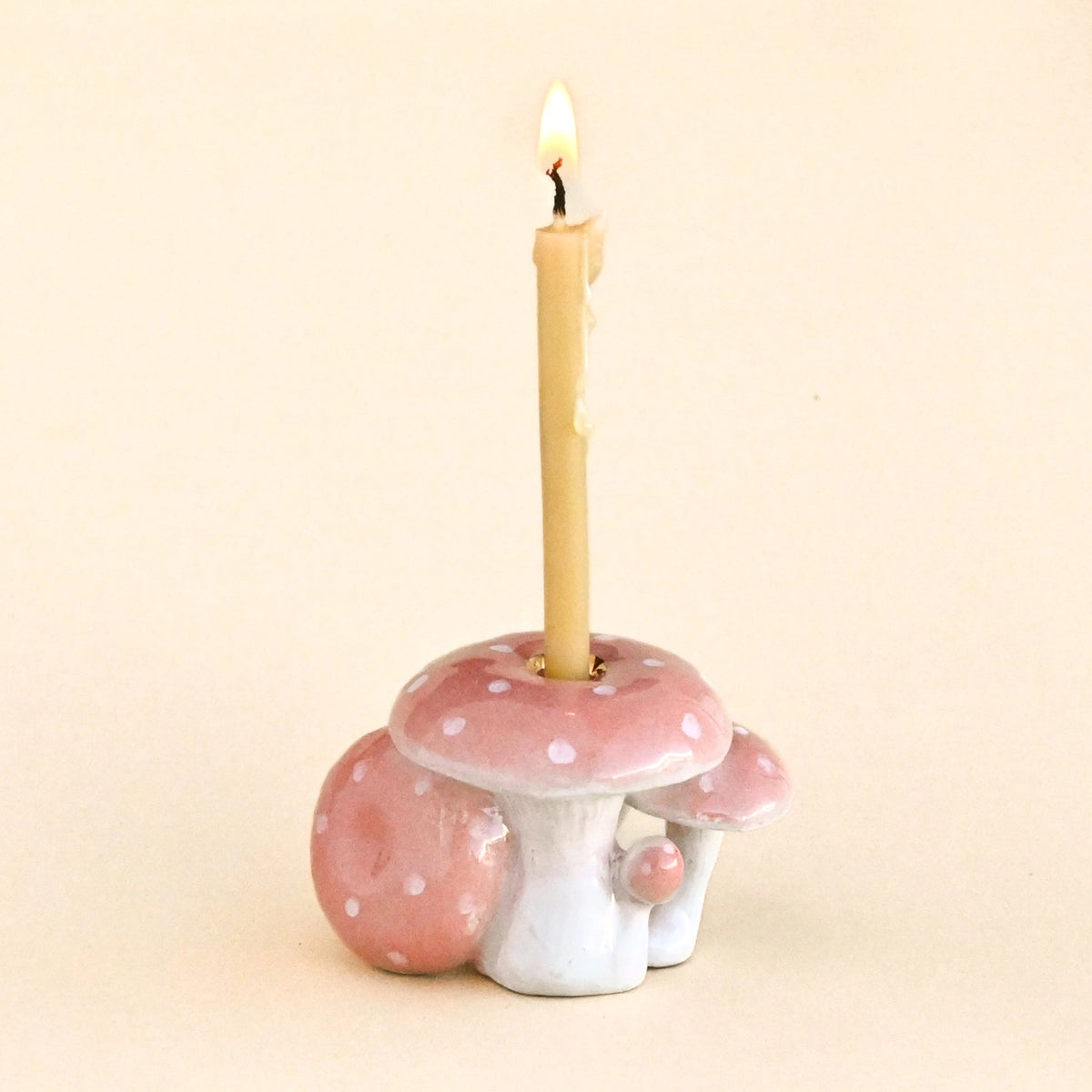 A small mushroom-shaped candle holder with a lit beige candle inserted into the center, photographed against a plain warm cream background.