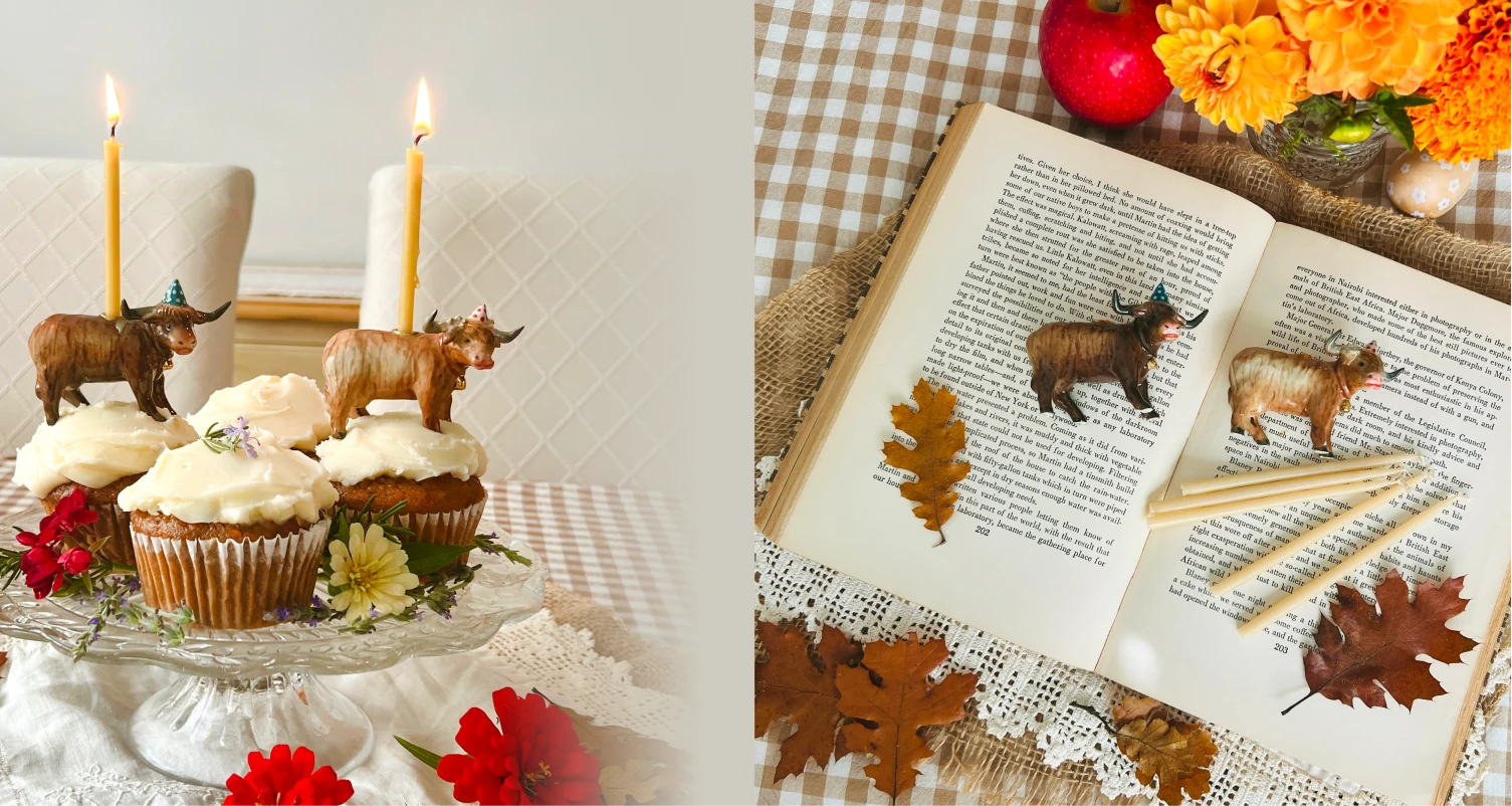 Highland cow birthday cake toppers on flower-decorated cupcakes and an open book with autumn flowers and candles