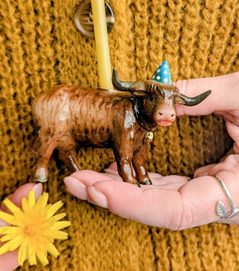 Porcelain Highland bull cake topper with a blue party hat and birthday candle